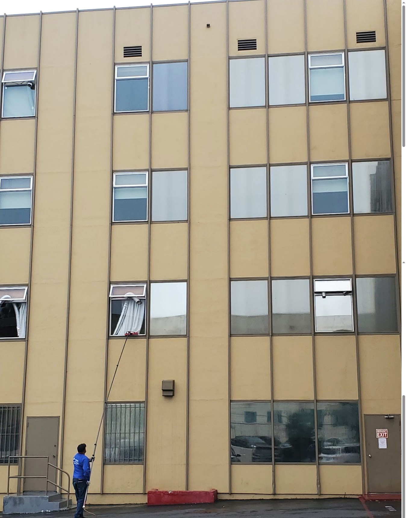 Technician using a water-fed pole for commercial window cleaning on a multi-story building