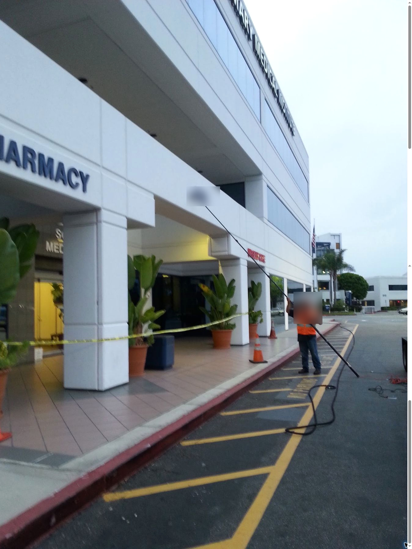 Technician cleaning upper windows at a medical property with cones and caution tape in place