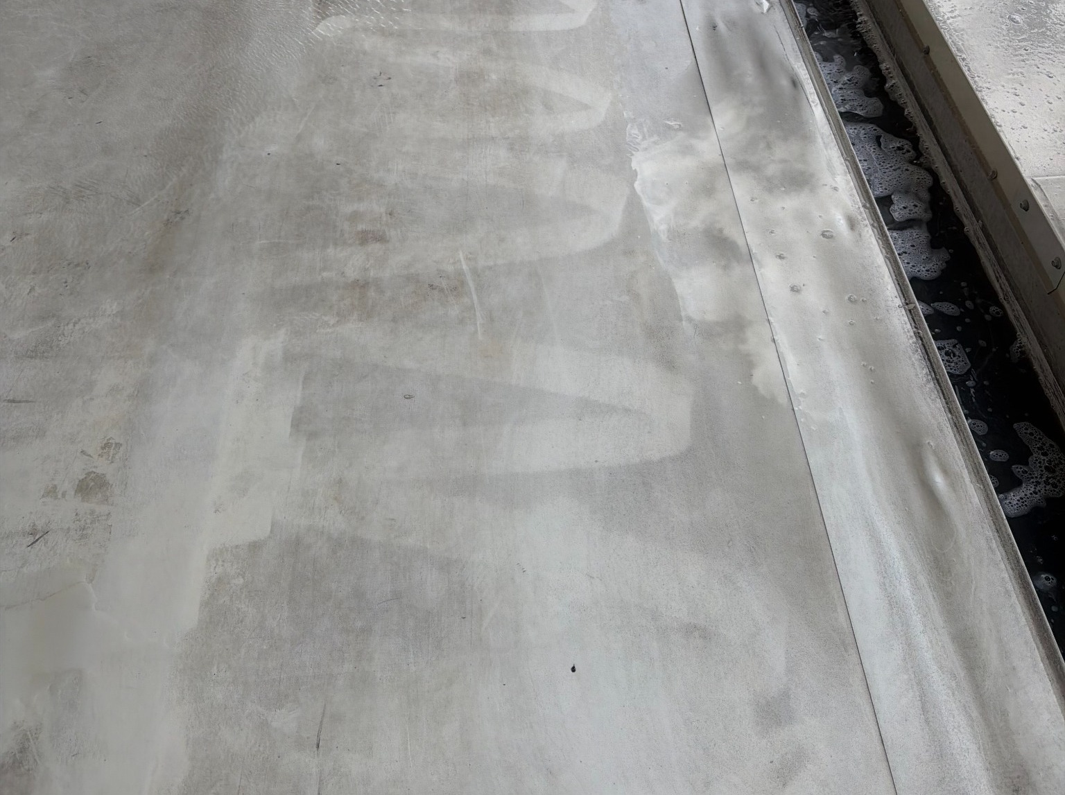 Gutter channel with water and bubbles beside a wet work surface.
