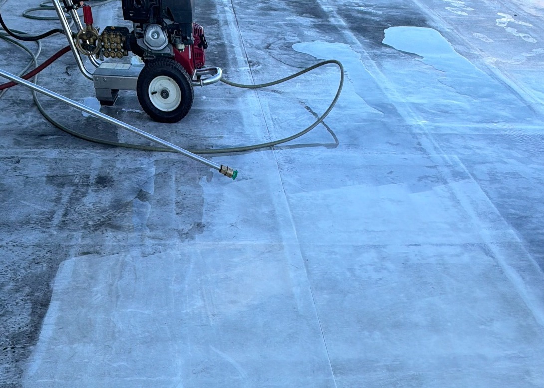 Wheeled pressure washer, hoses, and a pressure-washing lance on a wet work surface.